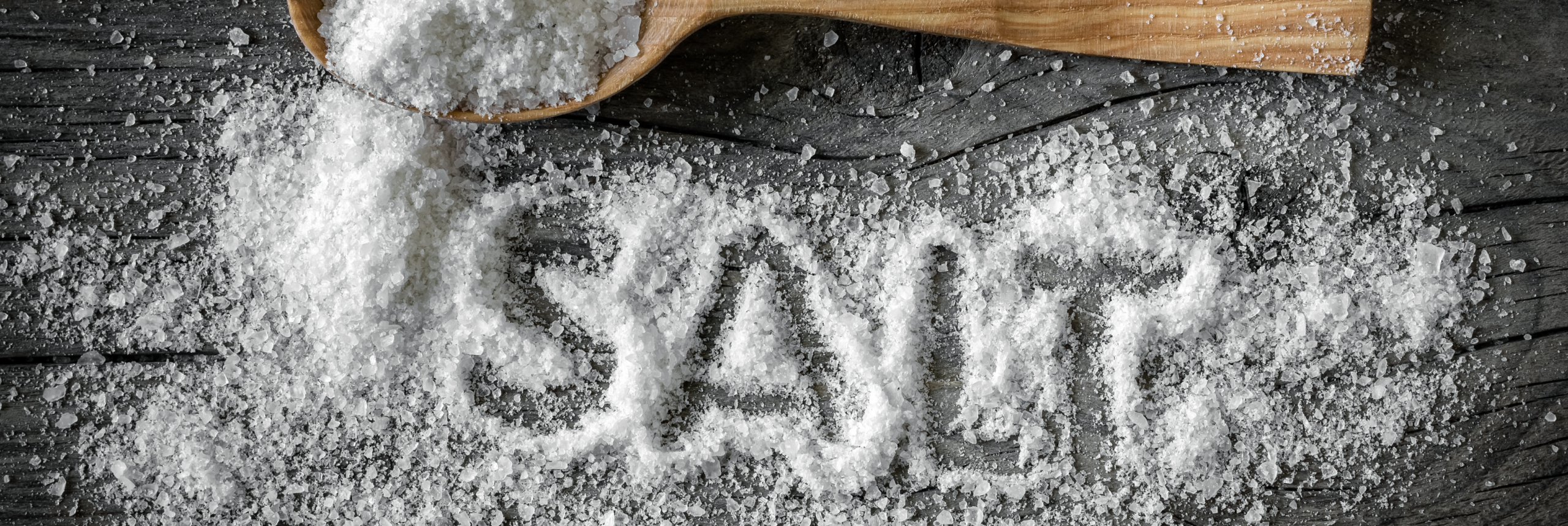 Salt on the table with a wooden spoon and the word SALT written in the salt.